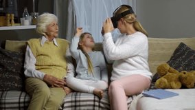 Woman watching video in VR glasses and then giving headset to little daughter while spending time with grandmother at home