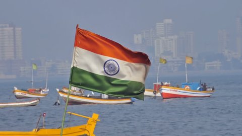 Slow motion shot of a waving Indian flag  installed on one of the fishing boats parked against city skyline, Mumbai, india