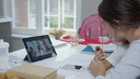 Mother having video conversation with colleague or relative via tablet computer and looking after three children at the same time