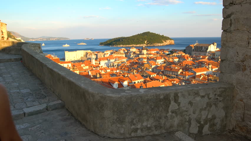 Woman traveller walk on the wall of Dubrovnik old town in Croatia. The Walls of Dubrovnik are series of defensive stone walls surrounding the city of Dubrovnik in Dalmatia region of Croatia.