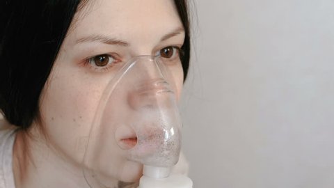 Use nebulizer and inhaler for the treatment. Closeup woman's face inhaling through inhaler mask. Front view