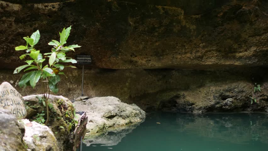 Athletic Young Tourist Man Jumping Into Natural Pool with Waterfall Water. Muscular Guy Extreme Bomb Diving in Clear Cave River. 4K, Slow Motion. Nusa Penida, Bali, Indonesia.