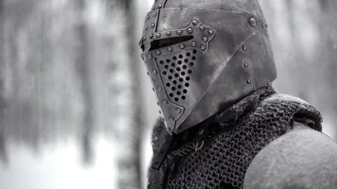 Portrait closeup of militant medieval knight wearing traditional steel armor and helmet, sword fighting in winter wood slow motion. Fantasy and reenactment
