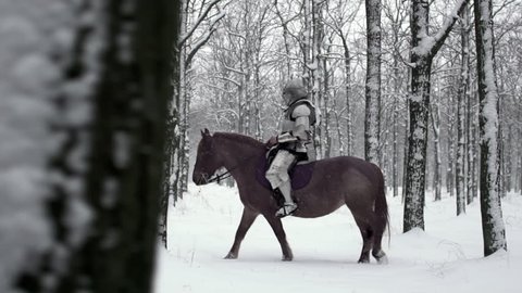 Portrait of medieval horseman wearing steel armor riding through winter forest, among snowy trees in slow motion. Reconstruction of ancient times