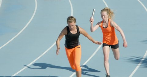 Two women running a relay race in slow motion pass the baton in slow motion.