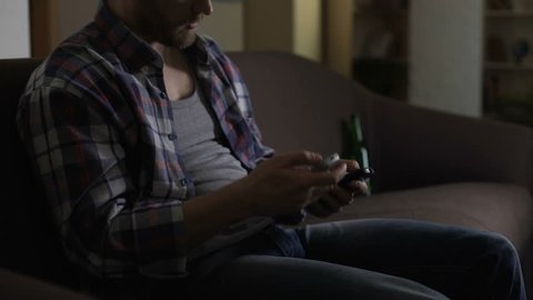 Male trying to switch TV channels with broken remotes, giving up, depression