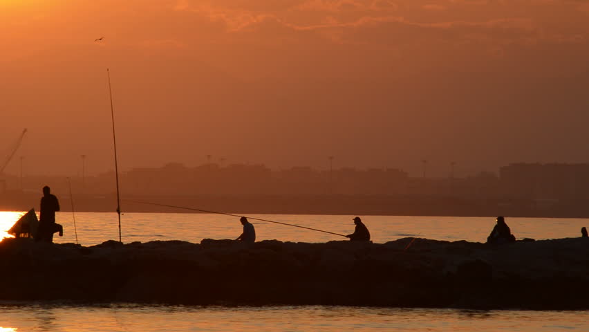 Silhouette of fishers fishing in the rocks at sunset