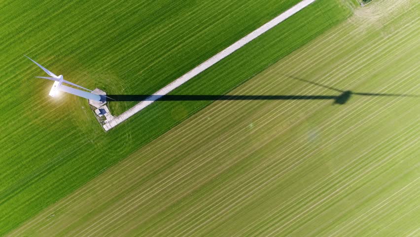 Aerial top down view wind turbine in polder landscape showing shadow from sun and sun reflection on top of construction wind turbine is device that converts winds kinetic energy into electrical energy Royalty-Free Stock Footage #1008306529