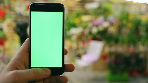man using smart phone in flower shop on blur background / bokeh light market public space business sell colorful flowers digital device tapping display mock-up swapping mobile green screen chroma key