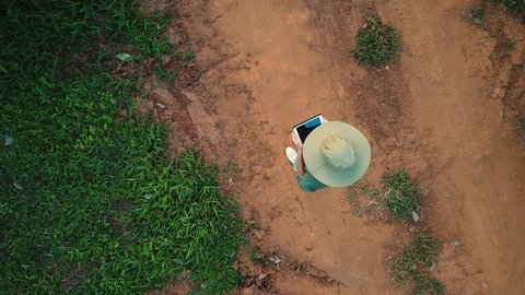 AERIAL. 100 meters up. Top view directly above a asian female farmer in the hat monitoring his farm with a tablet. Palms farm in Thailand.