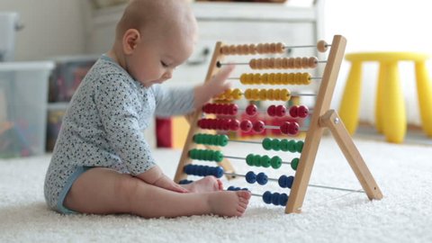 Cute little baby boy, playing with abacus at home, sunny kids room
