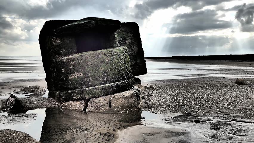 Machine gun bunker from World War 2 on a North Sea Beach in the East Riding of Yorkshire, England (covered in seaweed)Sun breaks through the clouds background. War relic. defences/bunkers scattered.