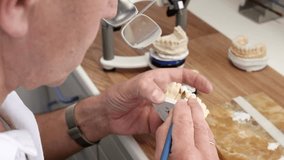 Dental technician in eyeglasses draws white ceramics glaze on prosthesis of teeth in workplace in laboratory of implants - Powered by Shutterstock - Get 15% off with code: PIKWIZARD15