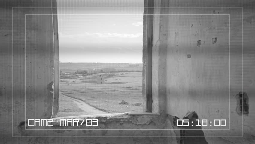 A CCTV camera screen: inside the ruins of an old abandoned house, a man goes near a window and looks outside.
