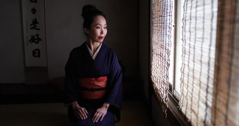 Portrait of Japanese woman wearing Kimono by traditional window looking to camera, Kyoto Japan