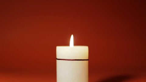 Christmas composition, with white candle lit on a red background.