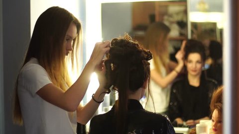 Young blonde stylist girl makes hairstyle to a woman in hair studio