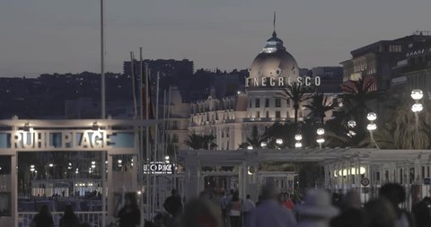 FRANCE, NICE,15 May 2017: Walking people at promenade des Anglais at evening, Hotel Negresco, car traffic, nights illumination, flag of France, famous white pavilion