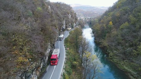 BOSNIA & HERZEGOVINA - NOVEMBER 2017: Tracking drone shot of petrol and logistics trucks driving over curvy road, through mountain gorge and along river, in Bosnia and Herzegovina, Southeastern Europe