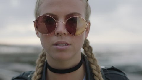 close up portrait of attractive blonde woman removes sunglasses looks confident to camera wearing leather jacket nose ring