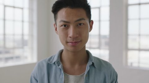 close up portrait of young asian teenager man looking serious confident at camera in apartment windows background slow motion