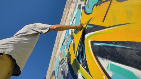 Graffiti artist is painting a yellow letter on the wall, view from below.