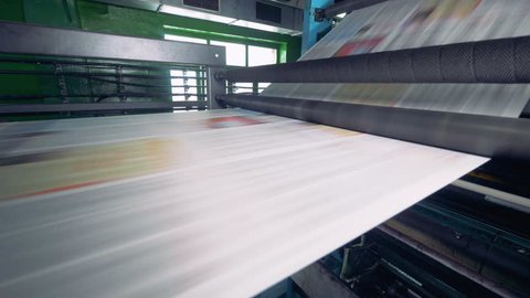 Newspaper strip on a printing machine. Detailed view on a printing machine in action. Newspapers passing near camera.