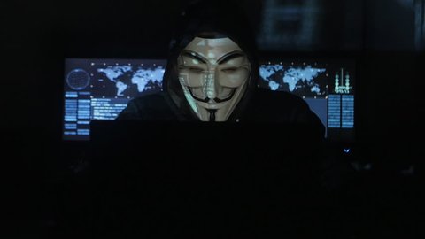 Cherkassy, Ukraine, January 23 2018: The hacker in the mask anonymus works in the data center. A programmer's portrait in Guy Guido Fawkes works at computer in dark room