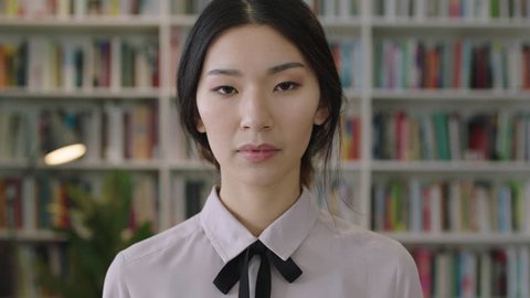 close up portrait of beautiful cute asian woman standing in library bookcase in background