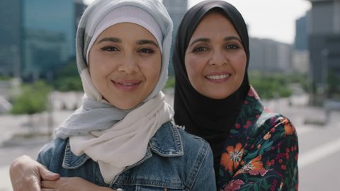 close up portrait of happy mother and daughter smiling cheerful hugging in urban city wearing traditional muslim hijab headscarf enjoying lifestyle culture family togetherness