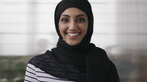 portrait of professional young muslim business woman looking at camera laughing cheerful wearing traditional headscarf in office background close up