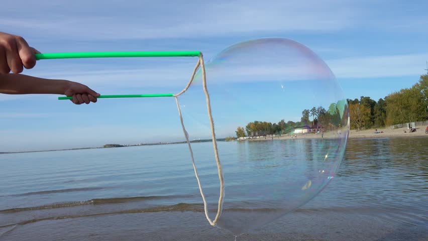 Young boy making big soap bubbles on the sea beach in sunny summer day