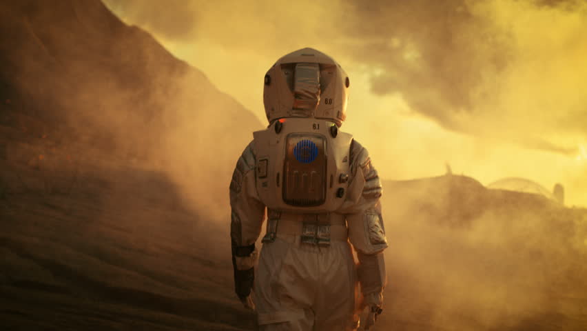 Following Shot of Female Astronaut in Space Suit Confidently Walking on Mars, Turing Around and Looking into the Camera. Red Planet Covered in Gas and Smoke. Shot on RED EPIC-W 8K Helium Cinema Camera