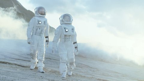 Two Astronauts in Space Suits Confidently Walking on Frozen Alien Planet, Exploration Expedition on the Planet's Surface. Space Travel, New Worlds Discovery, Colonization Concept. Slow Motion. 4K UHD.