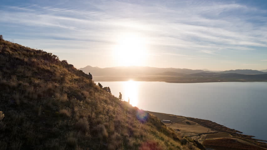 Aerial view flying past hikers climbing rocky path to view wide open landscape and lake at sunset. Royalty-Free Stock Footage #1008388156