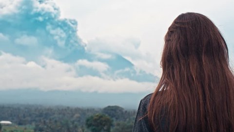 Rear view of tourist woman taking photo of Agung volcanic eruption, videoclip de stoc