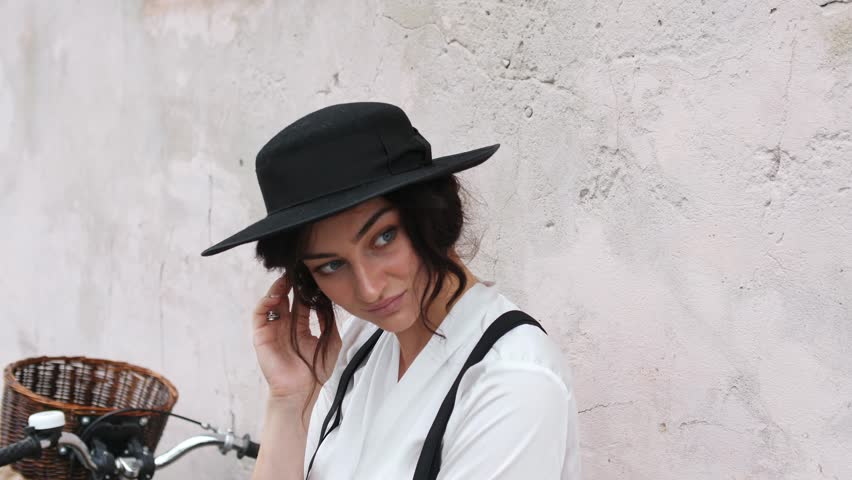 Close-up of a girl in a hat is standing by the wall with a bicycle.
