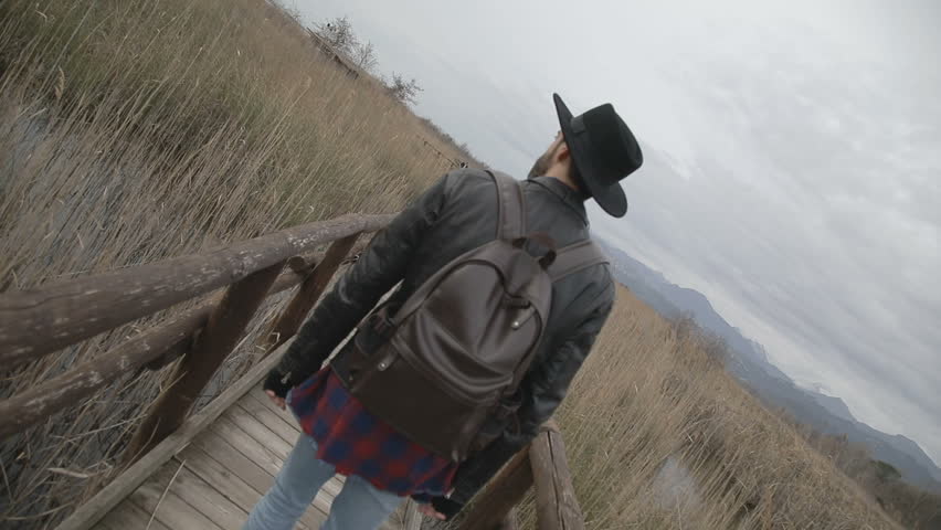 Boy with black jacket and hat is walking on the wooden bridge