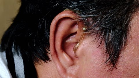 Asian man wearing a hearing aid on his right ear.