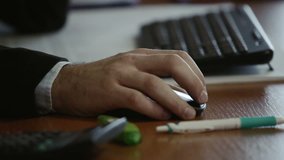 Close up video of a male business worker typing on a keyboard, clicking on a mouse and using a pen and eraser in an office environment.