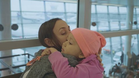 Yound mother and little cute daughter gently embrace at airport while waiting flight at departure lounge in slow motion.