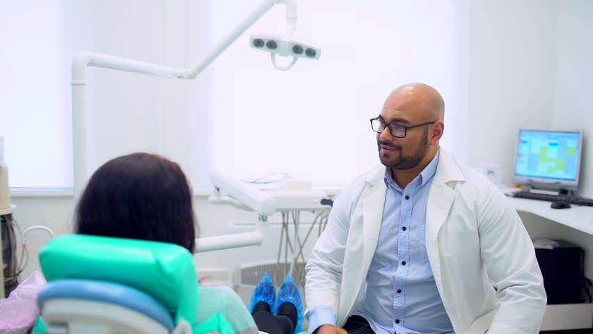 The kind man the dentist talks in a light office to the patient. slow-motion. Consultation of the dentist. A visit to the dentist's office. Royalty-Free Stock Footage #1008424009