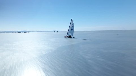 Sailing ship yacht skates on ice skate. Ice-boat sailing. Sport event competition on cold ice Russia North Asia Baikal. Winter frozen sunny snow day. Aeria together with. Drone high speed
