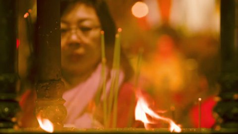 Taipei, Taiwan-10 February, 2016: An Asian woman is praying and burning incense sticks in a temple burner. There are flames and smoke.