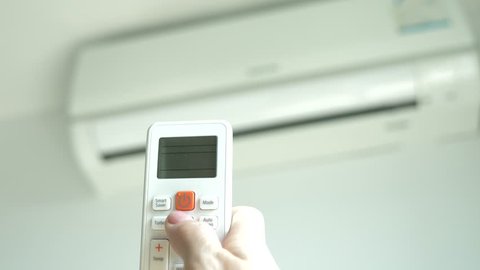 Air-conditioning is a wireless remote control in the hands for adjusting the room temperature. 4k, the hand pressing the buttons of the control panel on the background of the blurred air conditioning