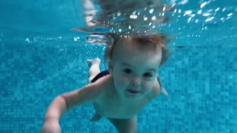 Happy baby boy diving under the water in the swimming pool. An underwater shot