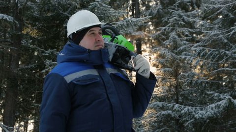 Worker with chainsaw on shoulder looking around in winter forest