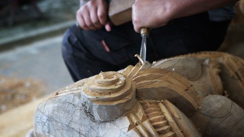 A close-up of a talented craftsman's hands using a chisel to carve a wooden Maori sculpture. 