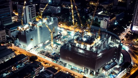 Time-lapse of construction site at night with light trails of traffic in the city, top view. Advanced building technology, busy metro downtown cityscape, or developing industrial country concept.