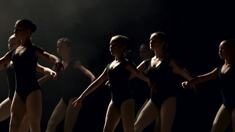 A group of young ballerina girls dancing on stage in the dark, close-up. A large group of children rehearsing and dancing the ballet.
